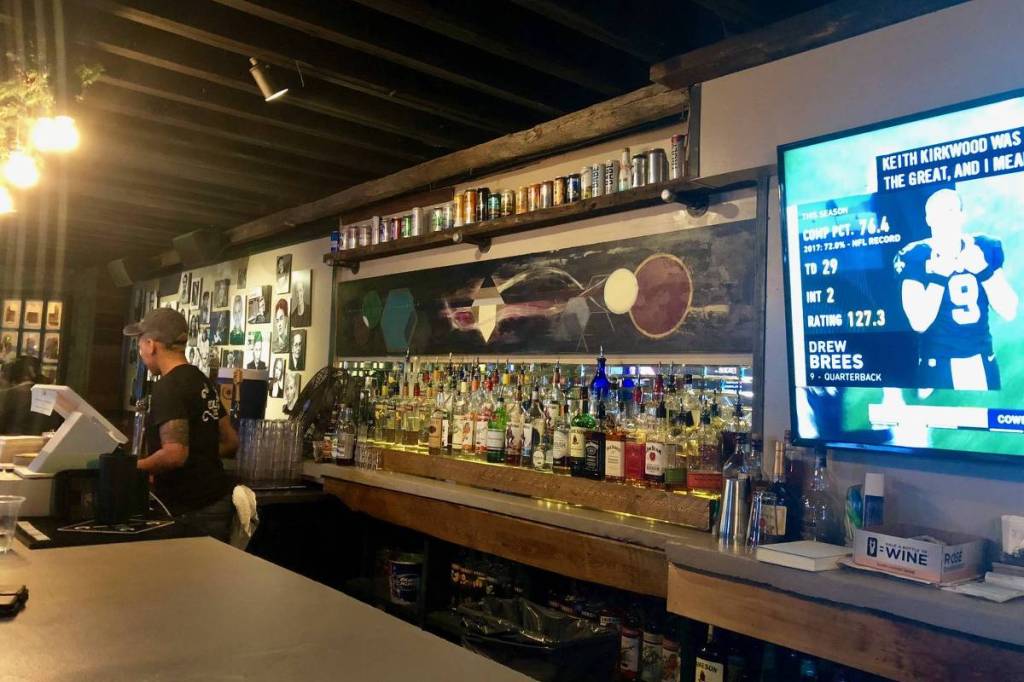 back bar of a gay bar showing an impressive row of liquor bottles beside a large screen TV showing American football